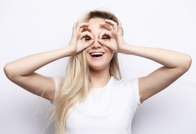 Lifestyle and people concept Happy excited young woman looking through hole made of her fingers over white background