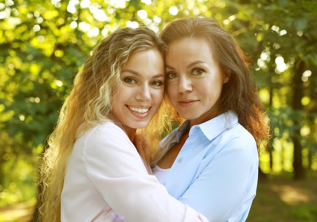 Lifestyle and people concept mature mother and adult daughter hugging in the park on a summer day