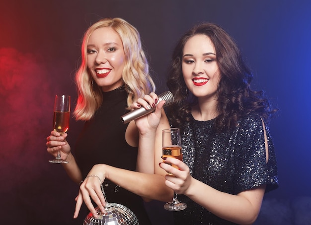 Lifestyle and people concept two beautiful young women with wine glasses and disco ball