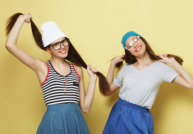 Lifestyle and people concept. Two young girl friends standing together and having fun on yellow