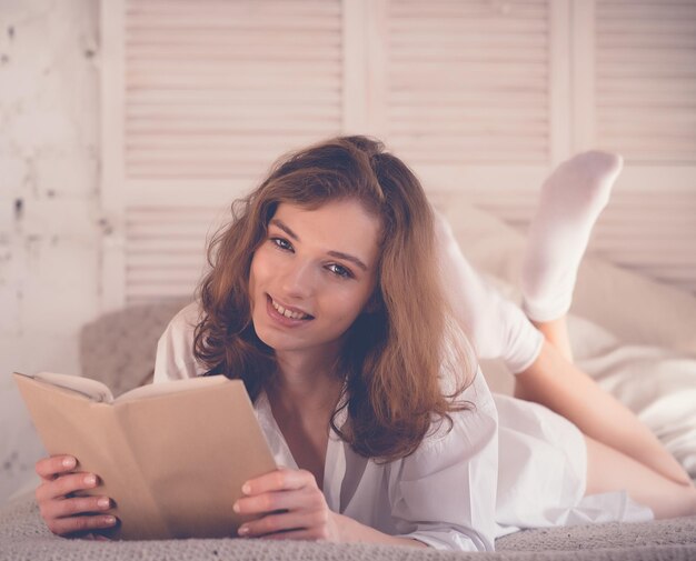 ライフスタイルと人々の概念読書しながらベッドに横たわっている若い女性