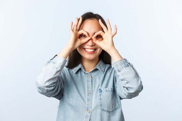 Stile di vita, emozioni delle persone e concetto di bellezza. sognante ragazza asiatica carina in abiti casual che non vede l'ora di studiare all'estero con un nuovo programma, mostra il segno ok o gli occhiali con le mani sugli occhi