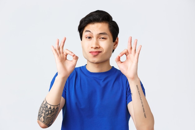 Lifestyle, people emotions and beauty concept. satisfied and totally pleased asian man showing okay perfection gesture and smile impressed, tasted fantastic tasty food, grey background