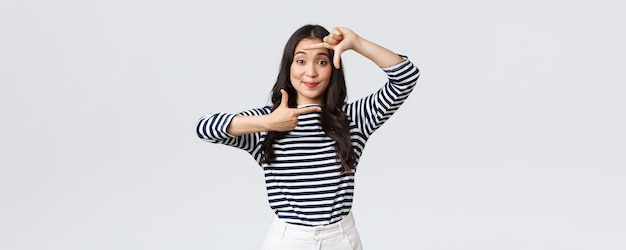 Lifestyle people emotions and casual concept Creative cute asian girl picturing capture moment with hand frames gesture smiling amused staying positive and happy white background