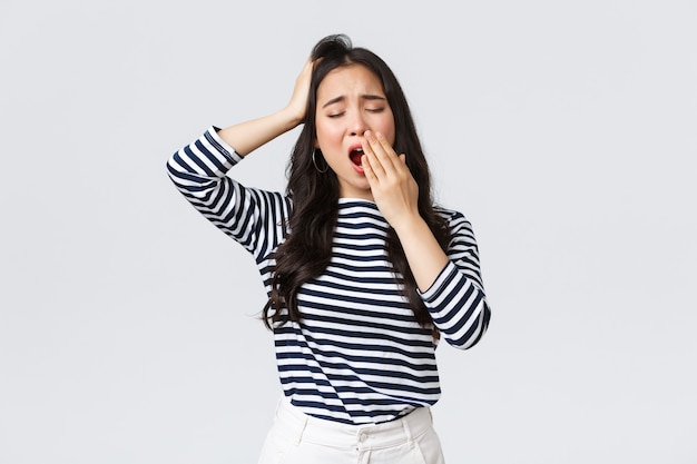 Lifestyle, people emotions and casual concept. Sleepy tired woman working late in office, close eyes and yawning, want go bad. Asian girl woke up early, need coffee, stand white background