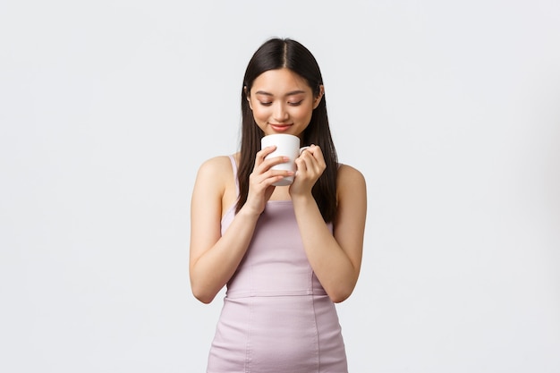 Lifestyle, people emotions and glamour concept. Sensual and romantic smiling asian woman, looking inside coffee cup dreamy, thinking