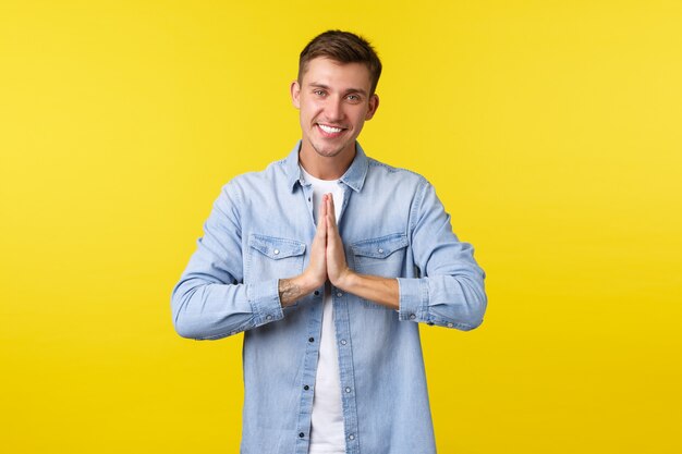 Lifestyle, people emotions and summer leisure concept. Friendly peaceful handsome happy man, smiling white teeth, thanking for help, hold hands in pray or namaste gesture, yellow background.