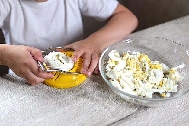 Lifestyle peuter kind meisje koken eten in de keuken. ontwikkeling van fijne motoriek in het dagelijks leven uit afvalmateriaal. het kind snijdt de eieren met een gele eiersnijder.