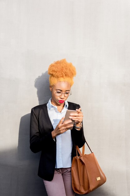 Lifestyle portrait of an african businesswoman in casual suit using smart phone on the gray wall background