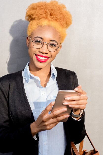 Портрет образа жизни африканской бизнес-леди в повседневном костюме с помощью смартфона на фоне серой стены