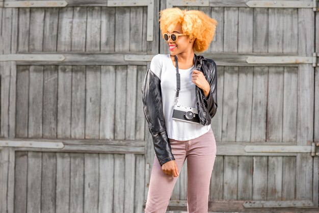 Photo lifestyle portrait of an african smiling woman in leather jacket talking phone on the wooden wall background