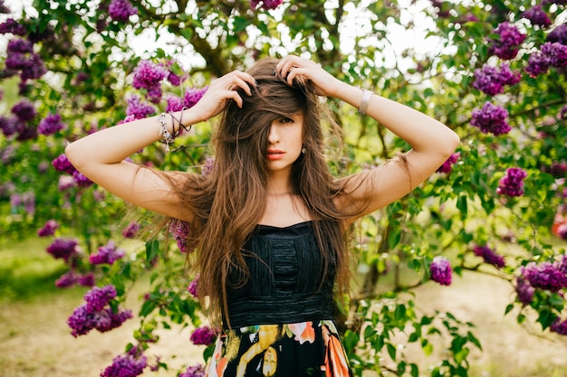 写真 ライフスタイルの肖像画美しい若いブルネットの少女彼女の長い髪を保持していると咲くライラックツリーの上ポーズ
