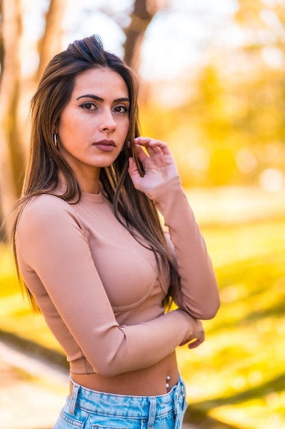 Lifestyle, portrait of a brunette model in a pink sweater and jeans walking in a park in autumn