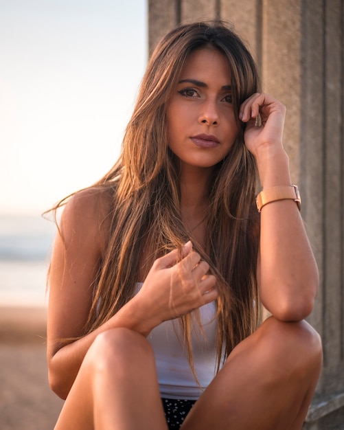 Lifestyle, portrait of a brunette in a white top sitting on the beach promenade on a sunset