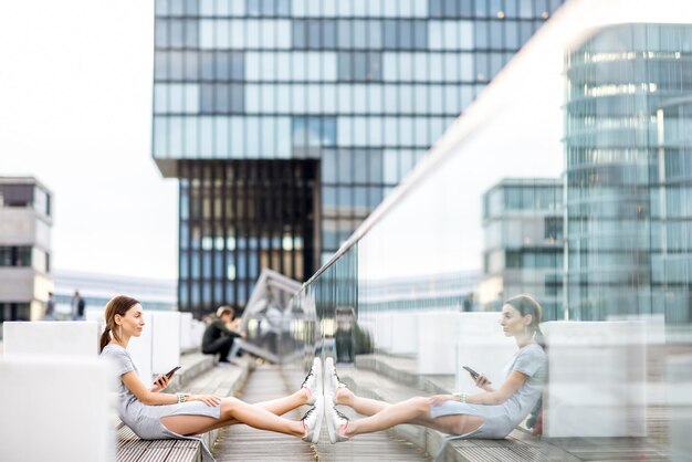 Lifestyle portrait of a business woman dressed casually sitting with phone outdoors at the modern district in Dusseldorf city, Germany