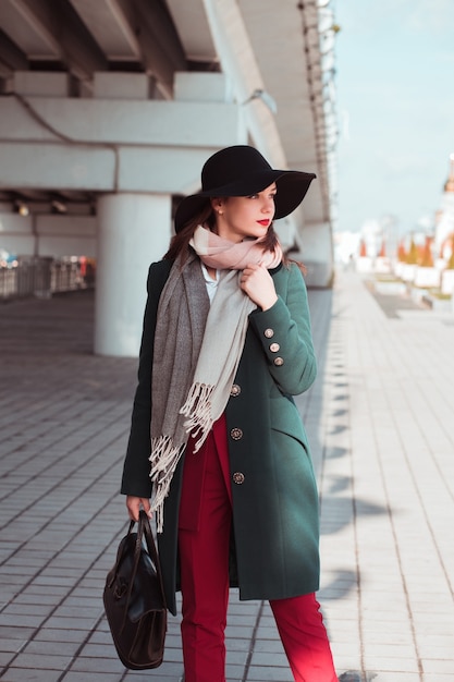 Lifestyle portrait of elegant brunette model wearing trendy outfit and holding woman's bag at the street.