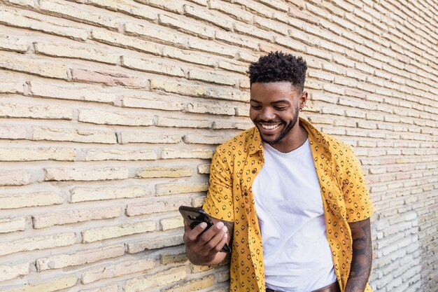 Ritratto di stile di vita di un bell'uomo americano utilizzando uno smartphone in strada con un muro di mattoni