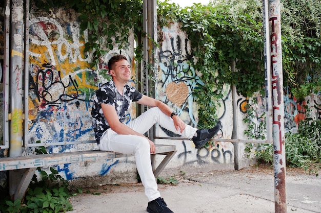 Lifestyle portrait of handsome man posing on the street of city with graffiti wall