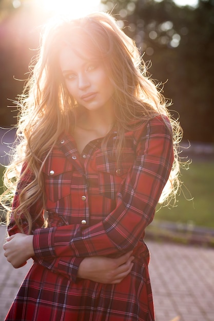 Lifestyle portrait of pretty young woman in dress posing in the city at sunset