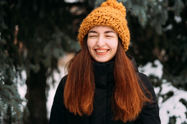 Lifestyle portrait of smiling millennial girl in orange hat. Snowy christmas day