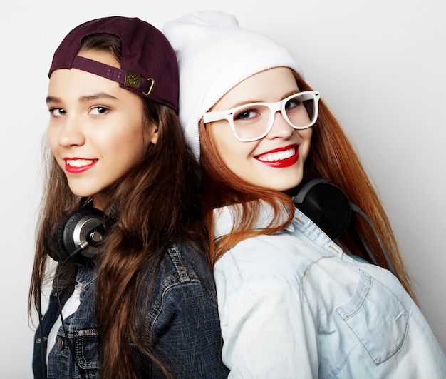 Lifestyle portrait of two pretty teen girlfriends smiling and having fun, wearing hipster clothes and hats, positive mood.