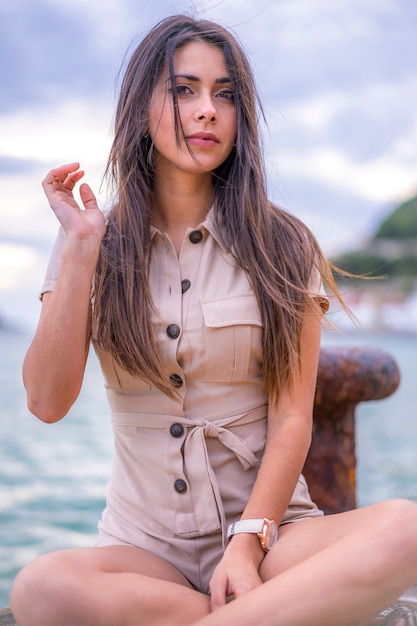 Lifestyle, portrait of a young brunette with brown overalls by the sea