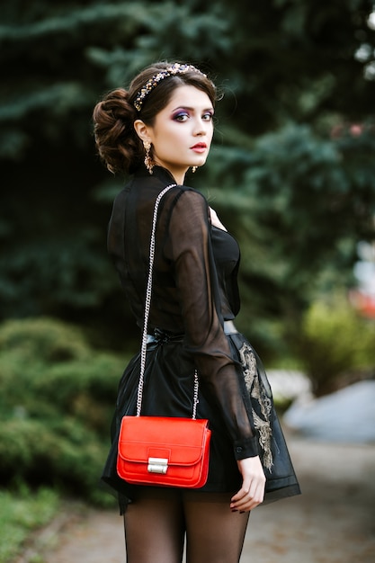 Il ritratto di stile di vita di giovane donna alla moda va in città con una borsa rossa alla moda.