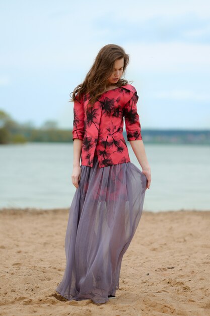 Photo lifestyle portrait of a young woman on the beach in transparent skirt and jacket with prints.