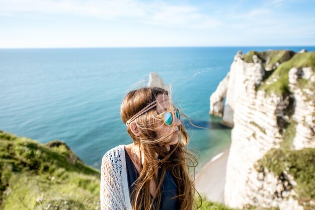 Lifestyle portrait of a young woman dressed in hippie style enjoying nature on the rocky coastline with great view on the ocean in France