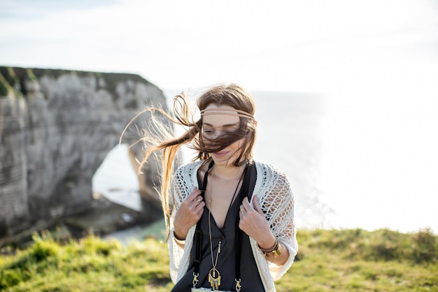 Lifestyle portrait of a young woman dressed in hippie style enjoying nature on the rocky coastline with great view on the ocean in France