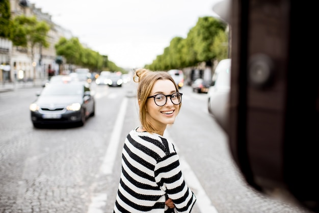 Lifestyle portrait of a young woman in striped sweater standing on the street in Paris