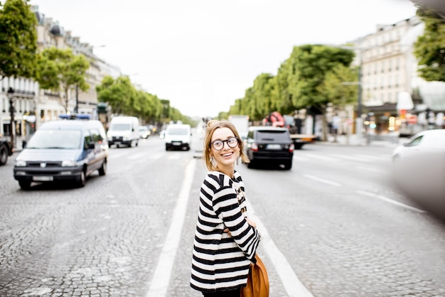 Lifestyle portrait of a young woman in striped sweater standing on the street in paris