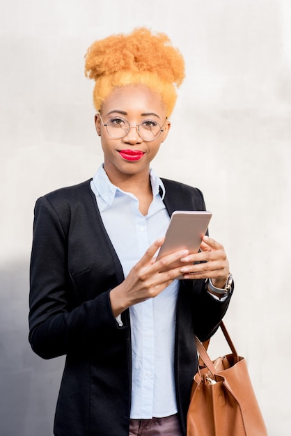 Lifestyle portret van een Afrikaanse zakenvrouw in casual pak met behulp van slimme telefoon op de grijze muur achtergrond