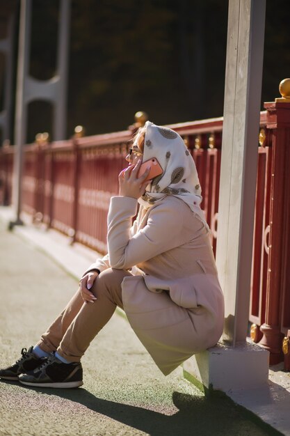 Foto lifestyle-portret van een mooi blond model draagt een beige jas, een witte sjaal en praat op haar mobiele telefoon