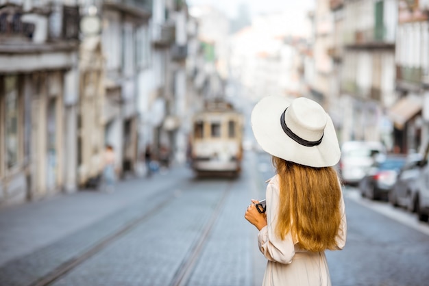 Lifestyle-portret van een vrouwelijke reiziger die op straat staat met de beroemde oude toeristische tram op de achtergrond in de stad Porto, Portugal