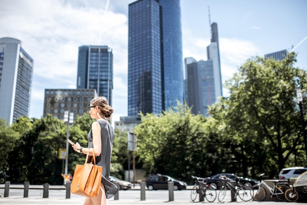 Lifestyle-portret van een zakenvrouw die met telefoon en tas loopt in de moderne wijk in de stad Frankfurt