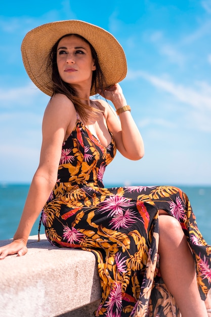 Lifestyle, a pretty young brunette in a dress and in a straw hat by the sea