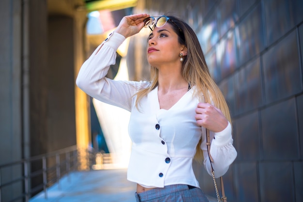 Lifestyle, a pretty young woman in a white shirt putting on sunglasses walking around the city