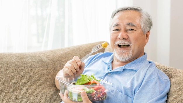 Lifestyle senior man feel happy enjoy eating diet food fresh salad on sofa