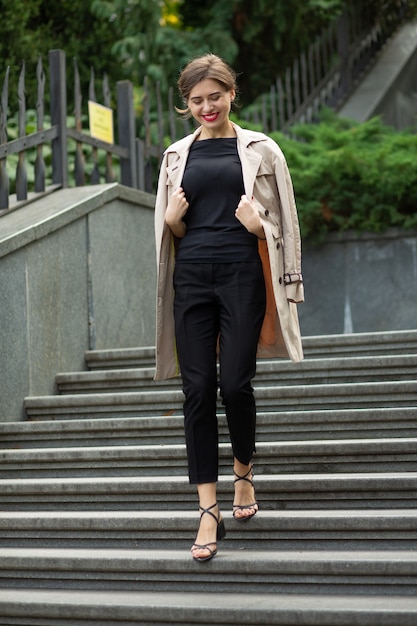 Lifestyle shot of a cheerful young woman with red lips and short curly hair wears trendy outfit going down the stairs