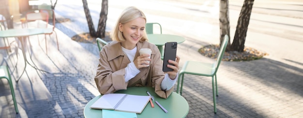 Photo lifestyle shot of stylish blond girl with smartphone drinking coffee posing with her chai for social