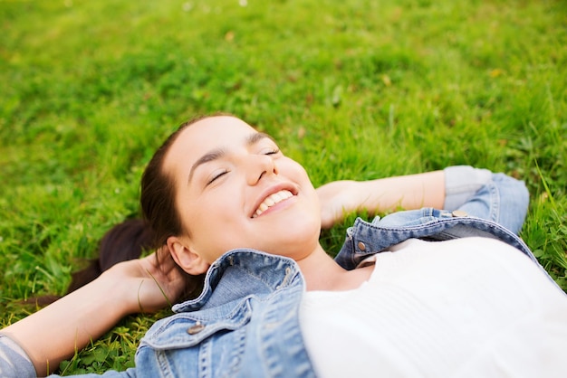 образ жизни, летние каникулы, досуг и концепция людей - улыбающаяся молодая девушка с закрытыми глазами, лежащая на траве