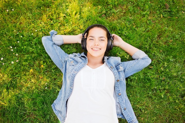 lifestyle, summer vacation, technology, music, leisure and people concept - smiling young girl in headphones lying with closed eyes on grass