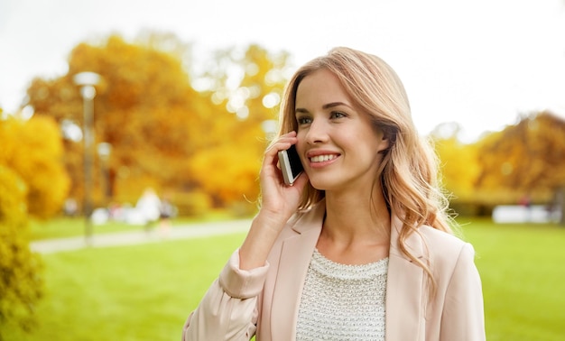 ライフ スタイル、技術、人々 のコンセプト - 秋の都市公園で屋外のスマート フォンで呼び出す笑顔の若い女性