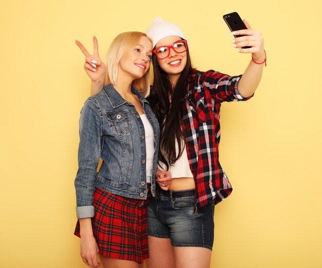 Lifestyle tehnology and people concept Happy girls with smartphone over yellow background Happy selfie