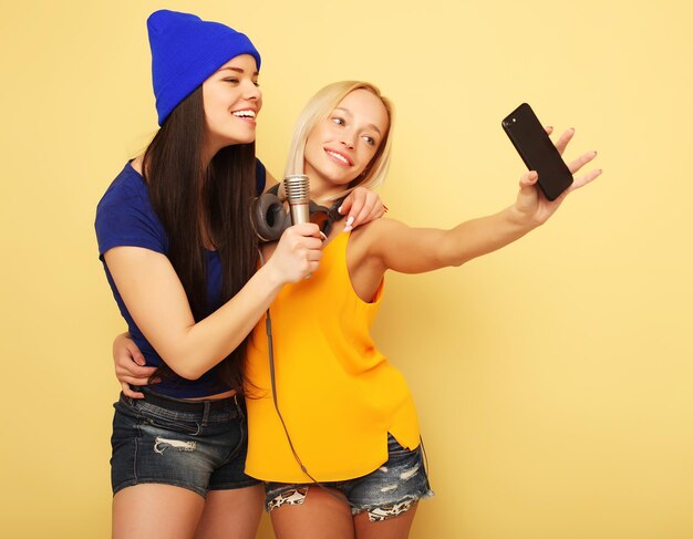 ライフスタイルの技術と人々の概念黄色の背景の上のスマートフォンで幸せな女の子幸せな自分撮り