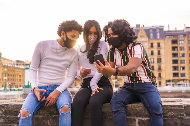 Foto stile di vita, tre amici che guardano i social network per strada con maschere facciali.