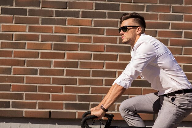 Фото Образ жизни, транспорт и концепция людей - молодой человек в солнечных очках на велосипеде по городской улице через кирпичную стену