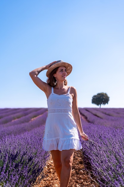 帽子をかぶった白いドレスを着て夏のラベンダー畑で微笑む女性のライフスタイル