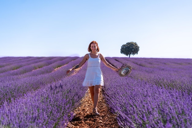 Stile di vita di una donna sorridente in un campo estivo di lavanda che indossa un abito bianco